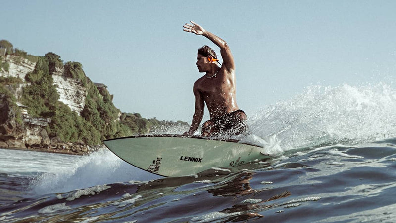 Raul Bormann surfing a wave wearing AONIC Flow bone conduction headphones