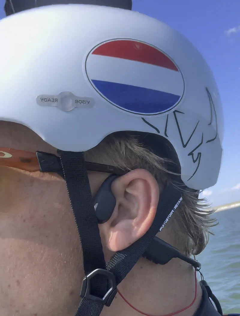 AONIC Flow bone conduction headphones fitting under a helmet strap, close up on the ear